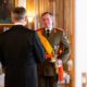 Ein Adjutant des Großherzogs in olivgrüner Galauniform mit roten Schulterklappen, orangefarbener Schärpe, Säbel und Mütze begrüßt einen Besucher im Großherzoglichen Palais — Photo: Cour grand-ducale
