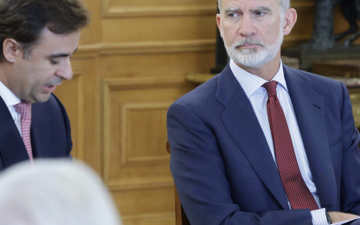 König Felipe VI. sitzend im Palacio de La Zarzuela in Madrid, dunkelblauer Anzug, gestreiftes Hemd und burgunderrote Krawatte mit Punkten, Papiere auf dem Schoß, zuhörend in einem holzgetäfelten Raum - Photo: @casareal.es