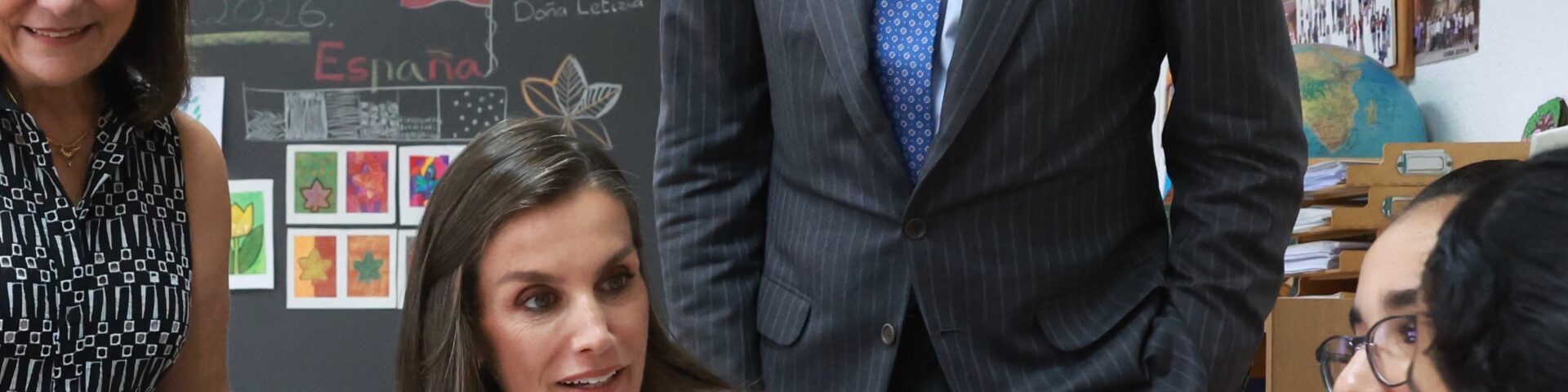 Königin Letizia in rosa plissierter Bluse sitzt an einem Schultisch und spricht mit Schülern der Schule Pintor Eduardo Morillas in Melilla, König Felipe VI. steht hinter ihr - Photo: @casareal.es