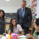 Königin Letizia in rosa plissierter Bluse sitzt an einem Schultisch und spricht mit Schülern der Schule Pintor Eduardo Morillas in Melilla, König Felipe VI. steht hinter ihr - Photo: @casareal.es