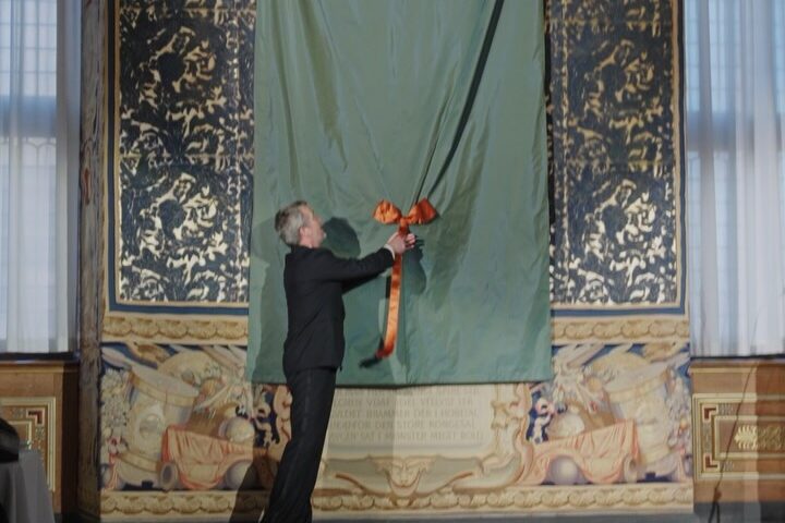 Die Enthüllung von König Frederik X.' erstem Porträt: Ein Mann im dunklen Anzug zieht an der Schnur der in grüne Seide gehüllten Leinwand im Rittersaal von Schloss Frederiksborg — Photo: Kongehuset