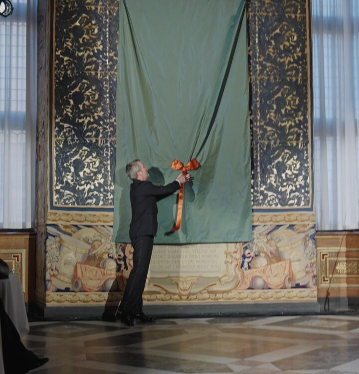 Die Enthüllung von König Frederik X.' erstem Porträt: Ein Mann im dunklen Anzug zieht an der Schnur der in grüne Seide gehüllten Leinwand im Rittersaal von Schloss Frederiksborg — Photo: Kongehuset