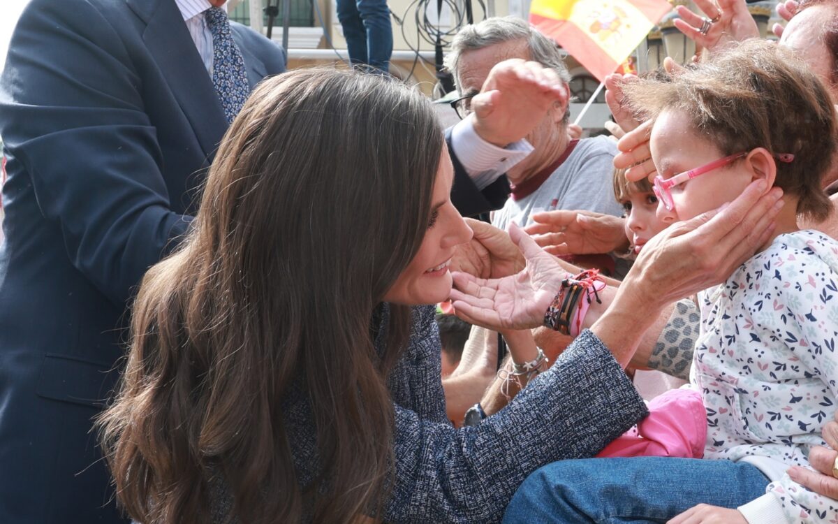 König Felipe VI. lächelt, während Königin Letizia in einer blaugrauen Jacke ein kleines Mädchen mit rosa Brille in einer jubelnden Menge mit spanischen Fahnen in Ceuta begrüßt - Photo: @casareal.es