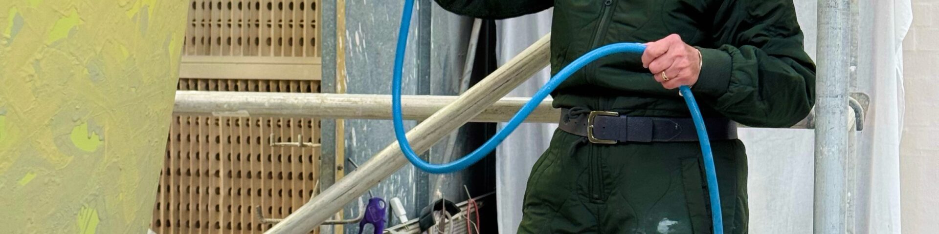 Königin Sonja glasiert in dunkelgrünem Arbeitsanzug und mit Maske auf einem Gerüst einen riesigen gelb-orangen Keramiktopf - Foto: Det kongelige hoff