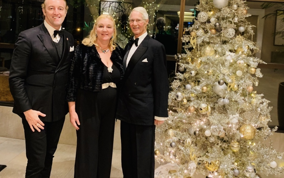 Prinz Mario-Max zu Schaumburg-Lippe mit zwei festlich gekleideten Gaesten neben einem gold geschmueckten Weihnachtsbaum in New York.