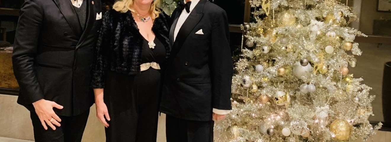 Prinz Mario-Max zu Schaumburg-Lippe mit zwei festlich gekleideten Gaesten neben einem gold geschmueckten Weihnachtsbaum in New York.