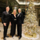 Prinz Mario-Max zu Schaumburg-Lippe mit zwei festlich gekleideten Gaesten neben einem gold geschmueckten Weihnachtsbaum in New York.