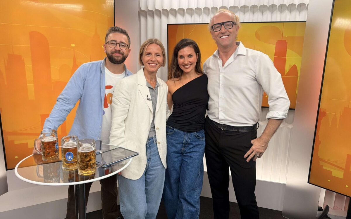 Prinz Mario-Max zu Schaumburg-Lippe im weißen Hemd mit Tania Rubis und Gästen im RTVI-Studio in Manhattan vor orangefarbenen Bildschirmen