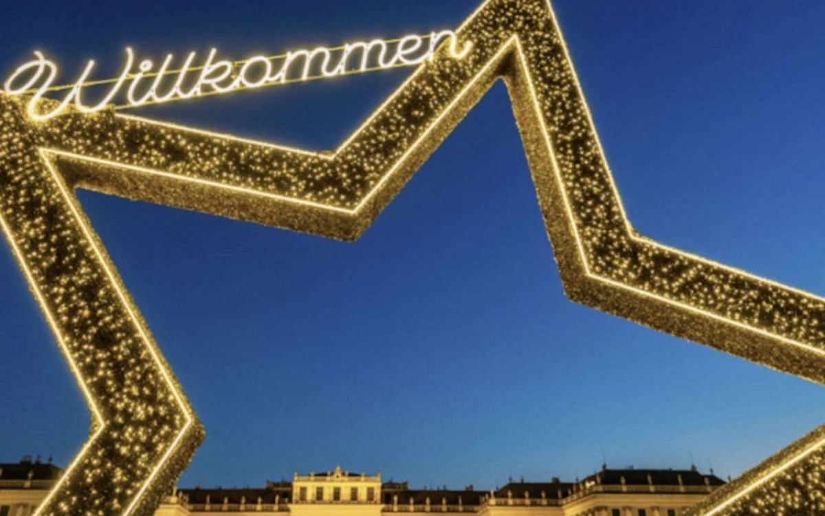 Der Weihnachtsmarkt vor dem hell erleuchteten Schloss Schoenbrunn in Wien in der Abenddaemmerung.