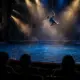 Luftakrobatin über einem riesigen Wasserbecken während einer Cirque-du-Soleil-artigen Aquatik-Show vor Theaterpublikum