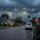 Vorstadtstraße in der Abenddämmerung unter Sturmwolken mit Übertragungswagen und mysteriösen Lichtern am Himmel