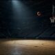 Basketball-Arena bei Nacht, ein Spotlight auf leerem Court, ein Basketball fliegt auf den Korb zu.
